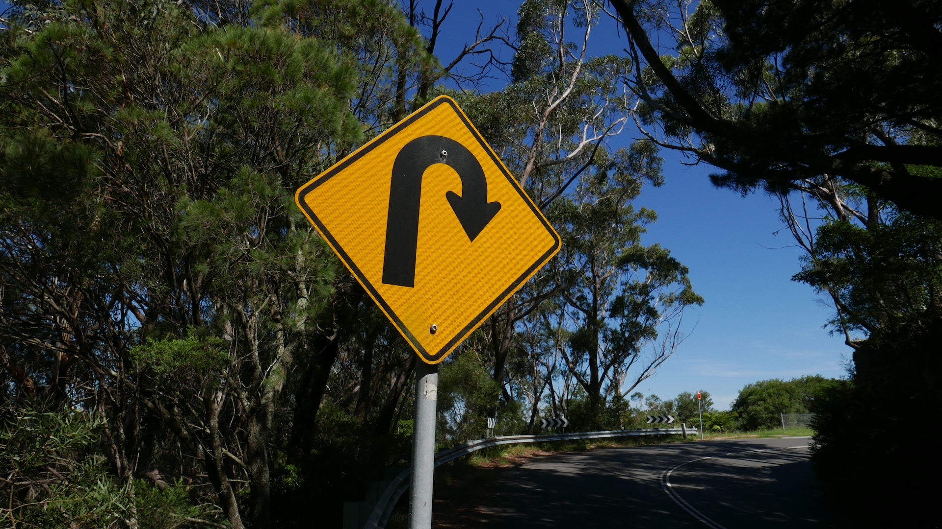 Photograph of a U-turn road sign, with trees and a road in the background. Photo by Jim Wilson on Unsplash.