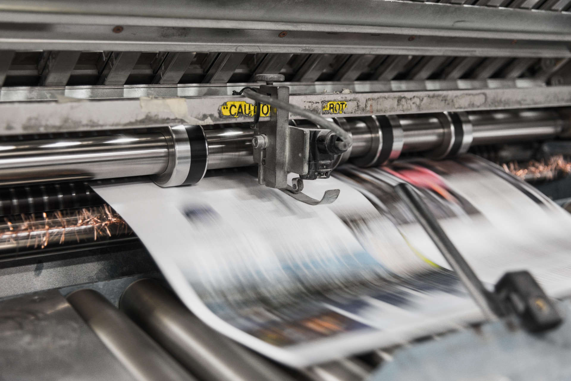 Description: image of newspaper moving through the printing press.  The pages are moving so quickly that they are a blur.  Photo by Bank Phrom on Unsplash.