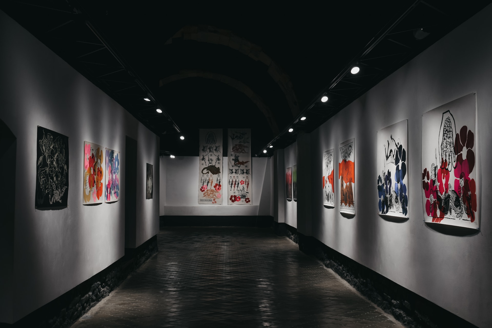 description: An image of a hallway in an art gallery. Colorful paintings hang on the walls to the left and right, and also on the wall ahead. Photo by Darya Tryfanava on Unsplash.